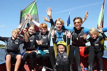 Groep kinderen op een boot, handen omhoog van het lachen